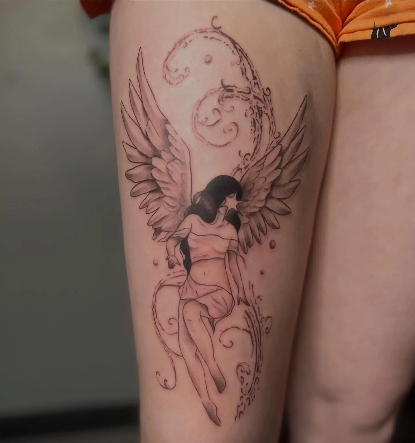 Fine line angel with wings and ornamental swirls on a thigh