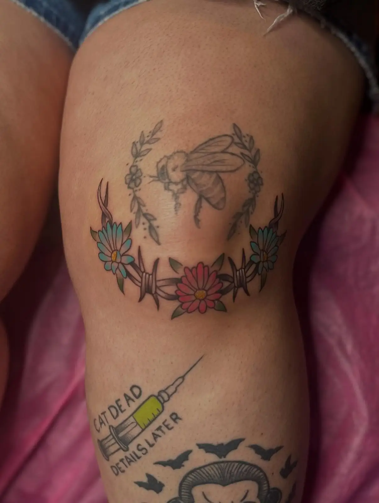 Bee and barbed wire daisy chain with colored flowers around a knee