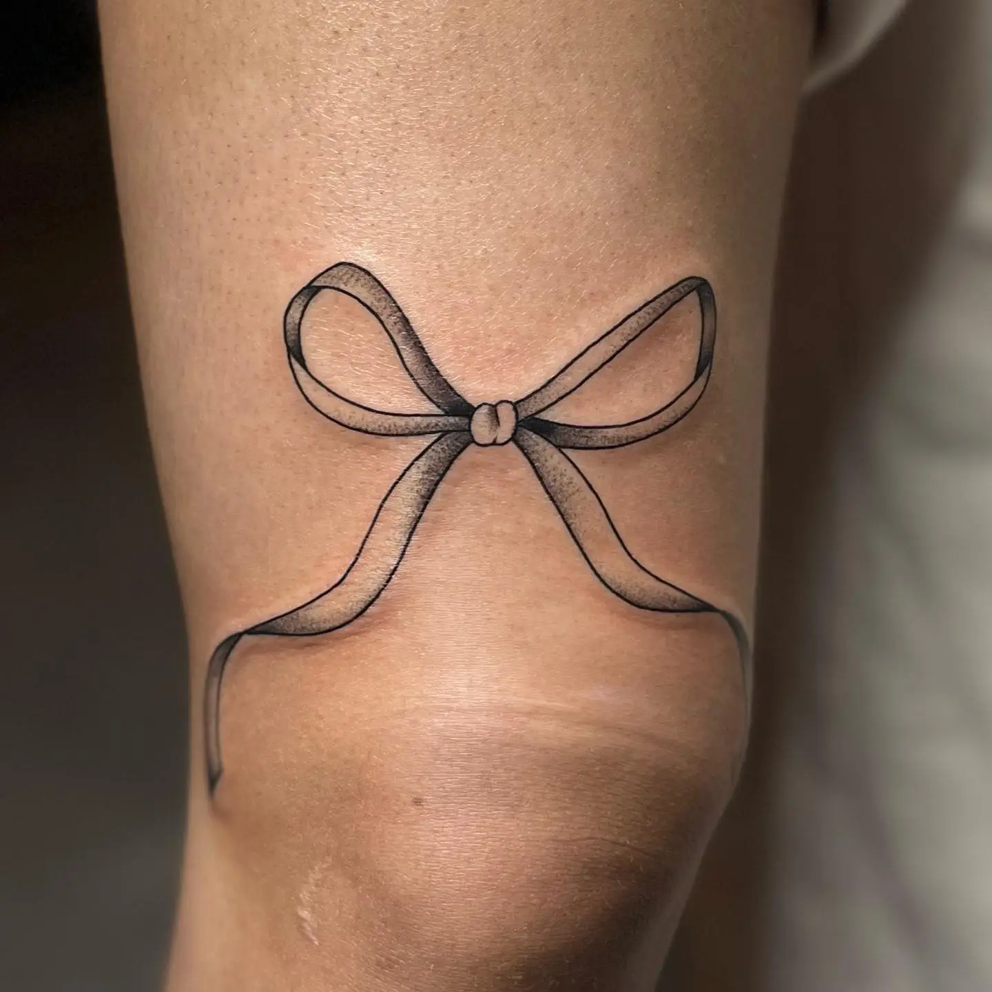 Fine line ribbon bow above a knee