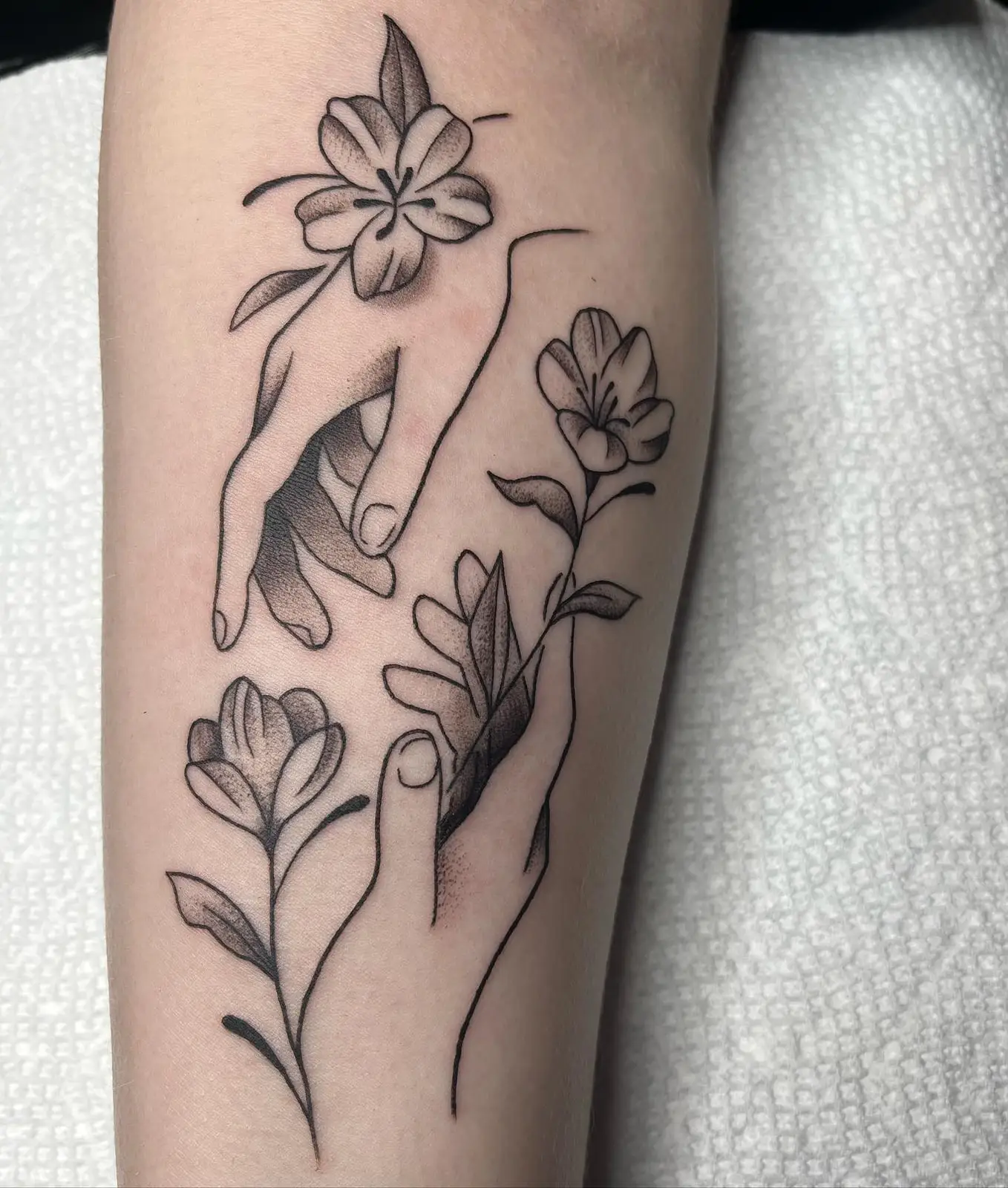 Fine line hands holding flowers on a forearm