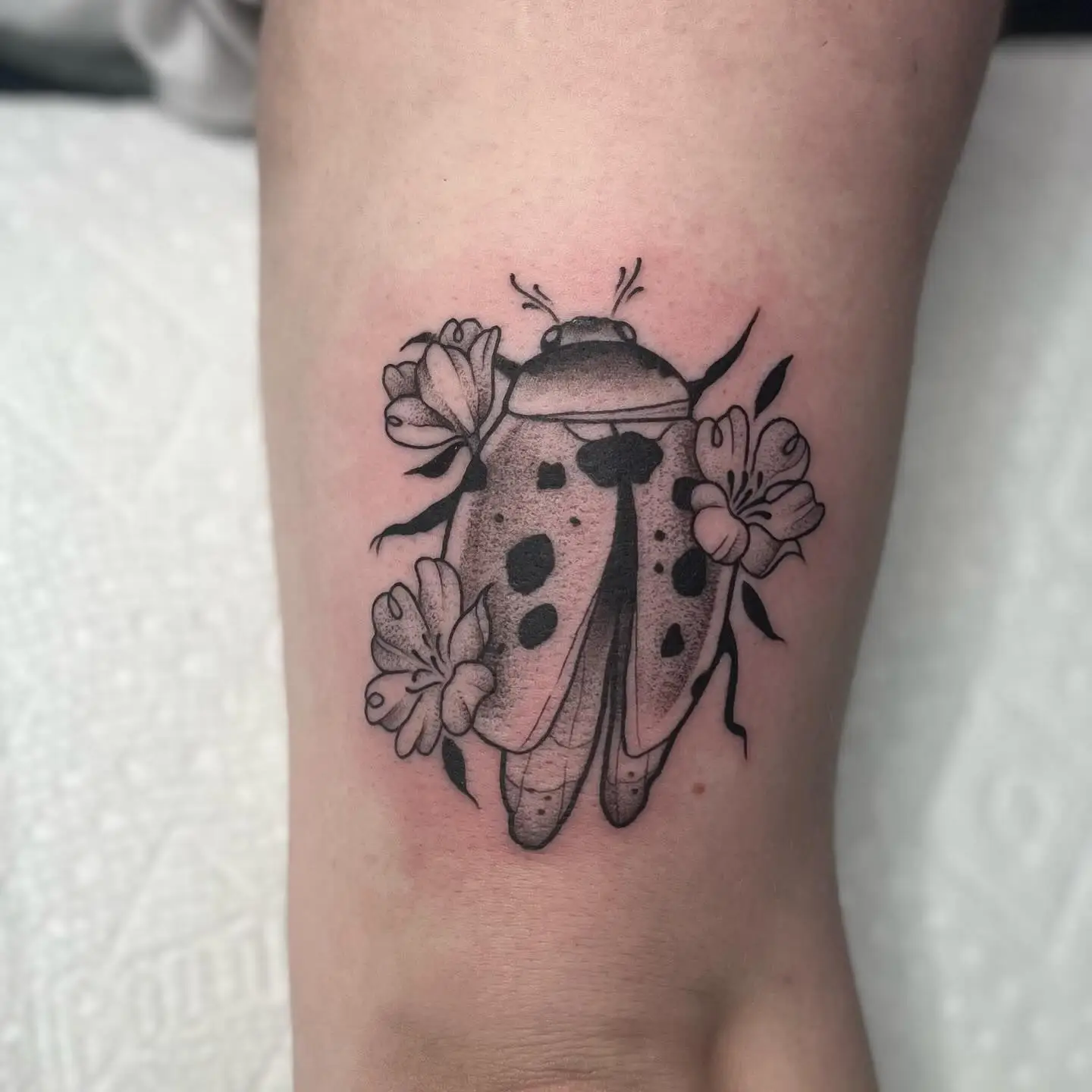 Stipple shaded ladybug tattoo surrounded by small flowers