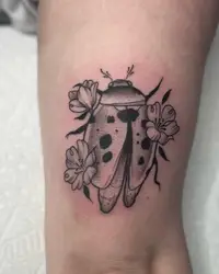 Stipple shaded ladybug tattoo surrounded by small flowers