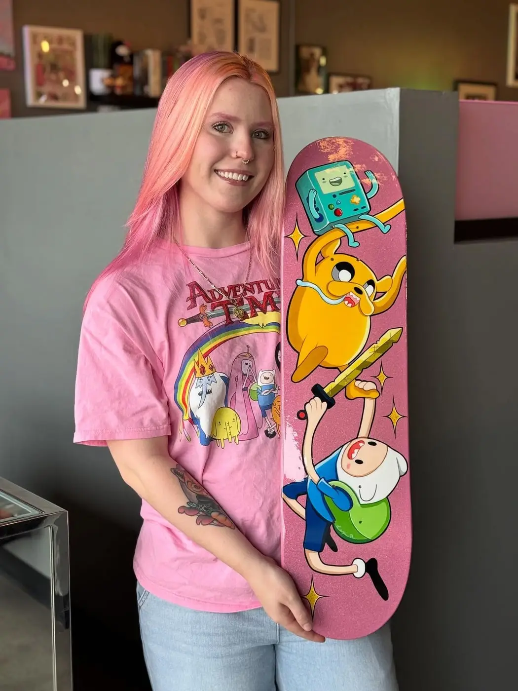 Tattoo artist Lexi Ross holding an Adventure Time skateboard she painted