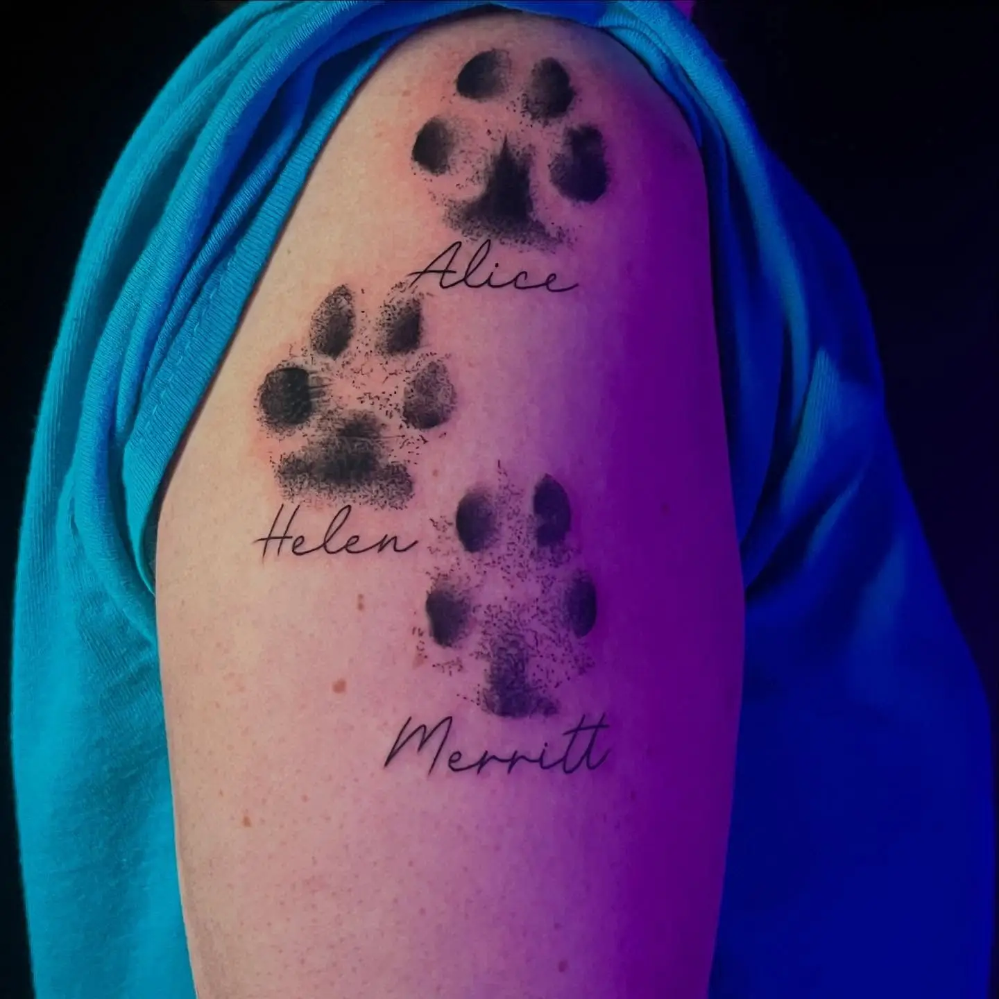 Three dog paw prints with names on an upper arm
