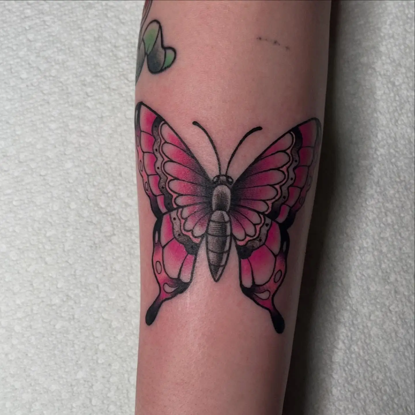 Bold traditional butterfly in pink and black on a forearm